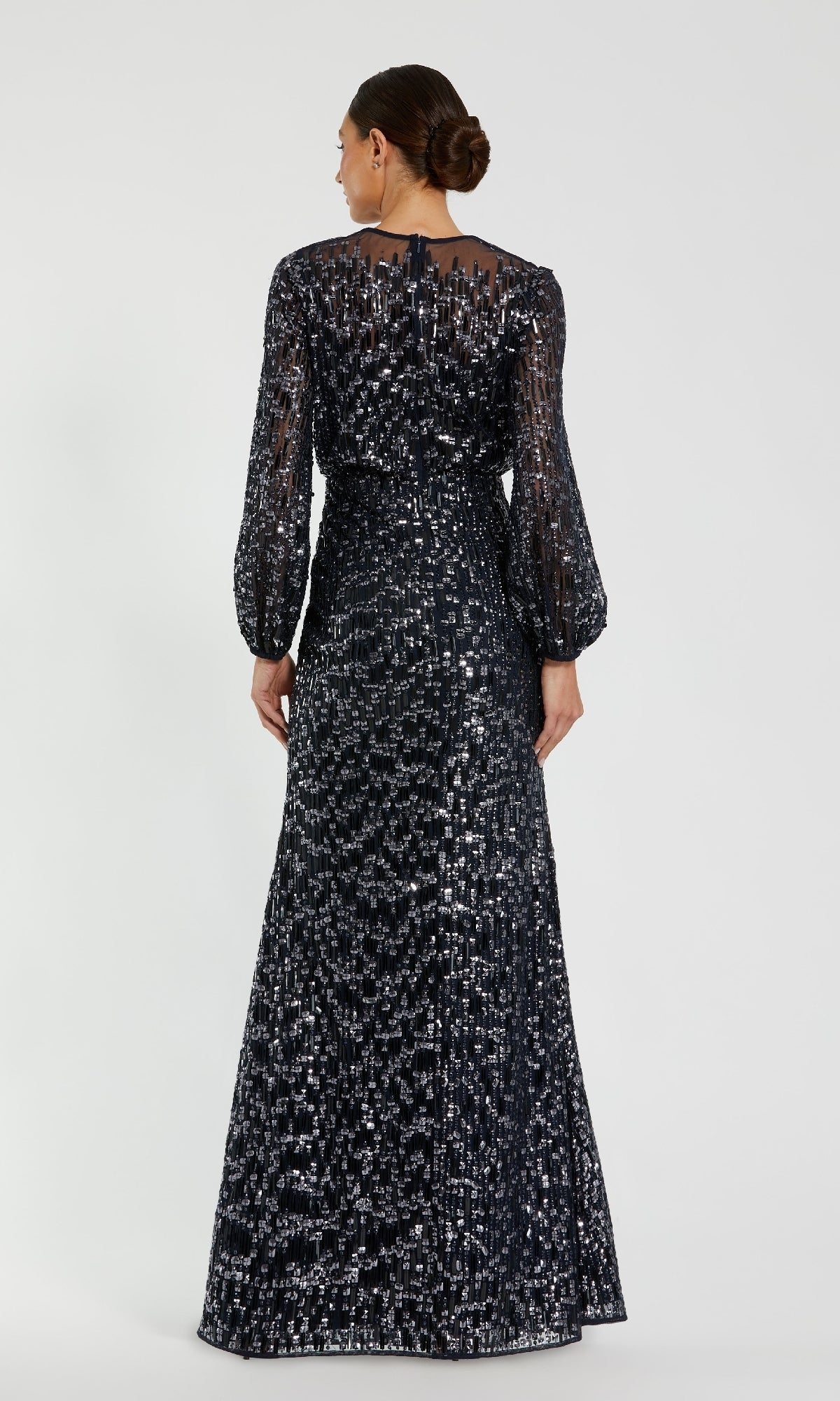 A woman with a low bun wears the Mac Duggal 94127 Long Sleeve Sequin Formal Dress—a black, floor-length gown with white sequins—shown from the back against a plain background.